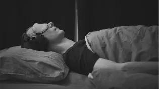 Man laying on bed with sound cancelling headphones and sleeping mask