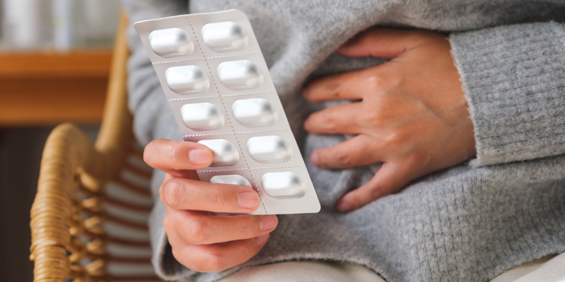 Close up of someone touching stomach and holding a packet of pills