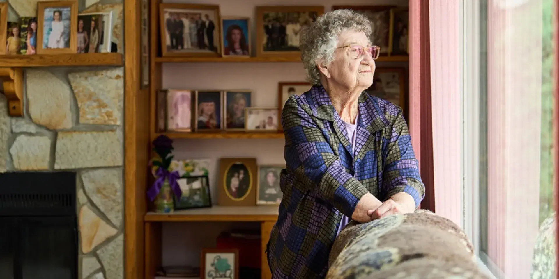 Elderly woman standing by sofa and looking out of window