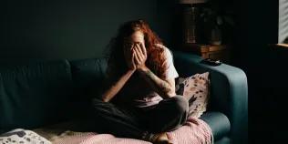 Women sitting cross legged on a sofa with hands covering face