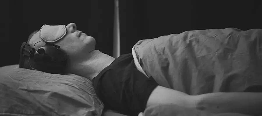 Man laying on bed with sound cancelling headphones and sleeping mask