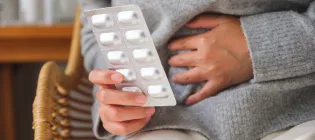 Close up of someone touching stomach and holding a packet of pills