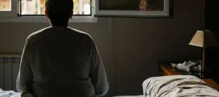 Back of person sitting on a bed looking out of a window