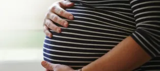 Close up of woman in stiped top cradling pregnant belly