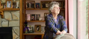 Elderly woman standing by sofa and looking out of window