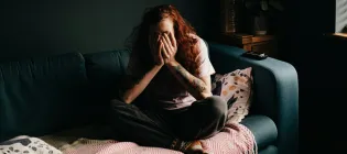 Women sitting cross legged on a sofa with hands covering face
